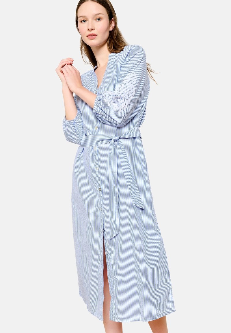 Abito camicia a righe blu e bianche con cintura, bottoni sulla parte anteriore, maniche a tre quarti e dettaglio ricamato sulla manica sinistra.