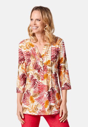 Langsleeve tuniek van lichtgewicht stof met een crèmekleurige achtergrond en rode en oranje bladeren patroon. V-hals met knoopdetails.
