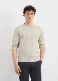 Pull à col rond beige à manches longues en tissu tricoté, doté de poignets et d'un ourlet côtelés, associé à un pantalon sombre pour un contraste.