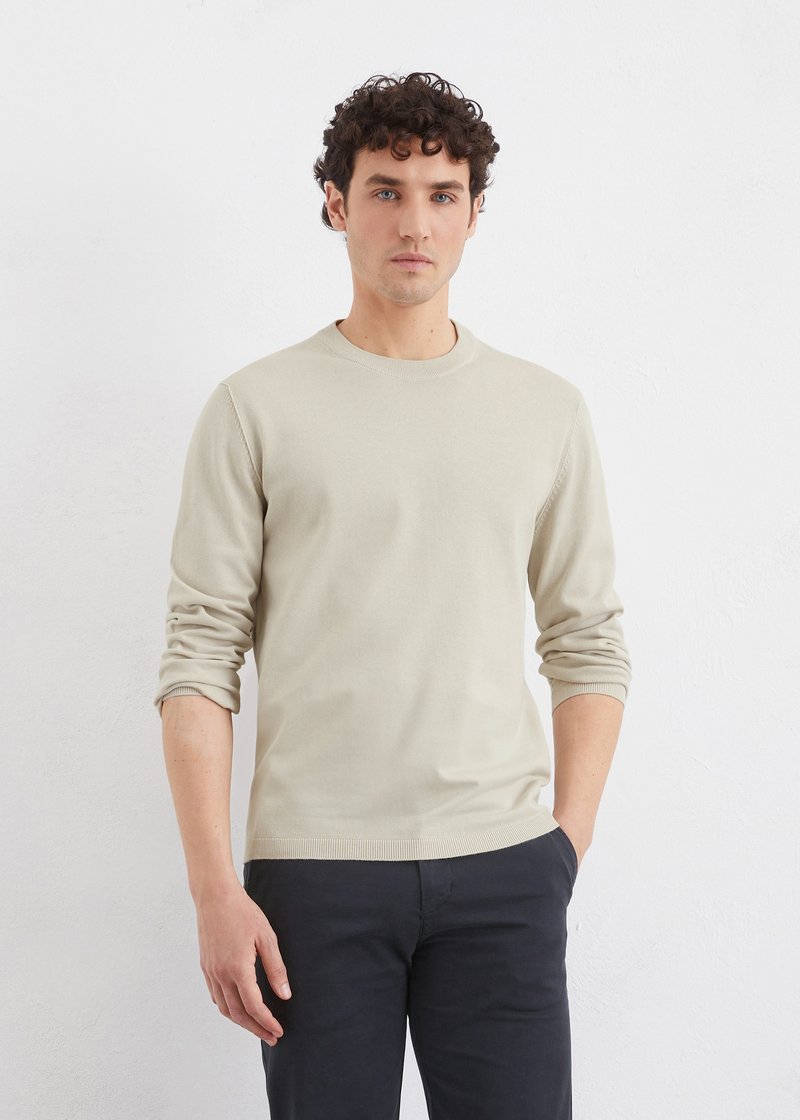 Pull à col rond beige à manches longues en tissu tricoté, doté de poignets et d'un ourlet côtelés, associé à un pantalon sombre pour un contraste.