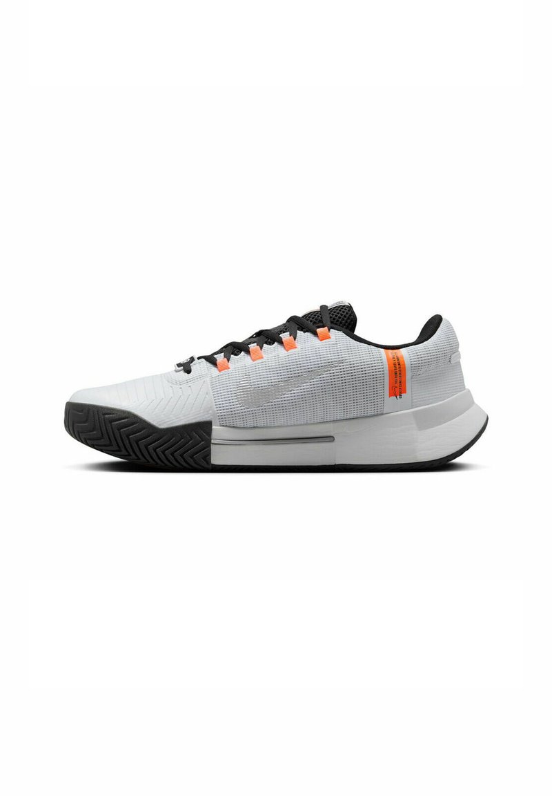 Białe buty sportowe z czarnymi akcentami, teksturowana siateczka z góry, pomarańczowe detale oraz podeszwa o wzorze zygzakowatym dla lepszej przyczepności. Niski profil.