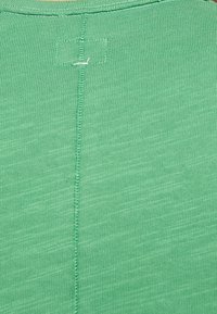Tissu vert présentant une texture côtelée, avec une couture centrale étroite et un petit détail de surpiqûre au niveau de l'encolure.
