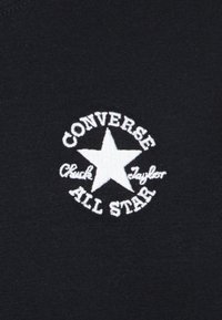 Čierna tkanina s bielym výšivkovým logom so hviezdou, na ktorom je napísané "CONVERSE Chuck Taylor ALL STAR", kruhový dizajn s textom.