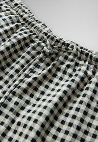 Nahaufnahme eines elastischen Bunds mit Kordelzug an Shorts aus schwarz-weiß kariertem Stoff.