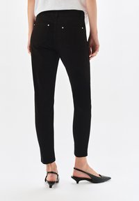 Czarne, wysokie dżinsy skinny z eleganckim fasonem, z tylnymi kieszeniami i subtelnymi detalami z metalu. Połączone z czarnymi, skórzanymi klapkami na obcasie.