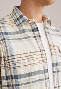 Flannel shirt featuring a white base with blue, brown, and black plaid patterns, a pointed collar, and buttons along the front.