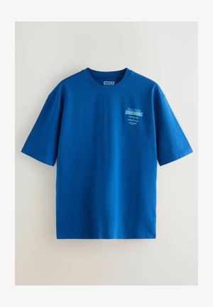 Zila kokvilnas t-kreklus ar īsām piedurknēm, ar balta logo drukājumu kreisajā krūtīs. Gluda tekstūra un brīva piegriezuma forma.