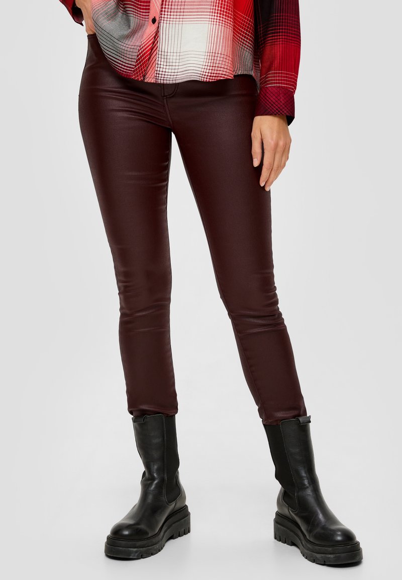 Pantalones de imitación de cuero burdeos con un diseño ajustado, que presentan una textura suave, corte slim y se combinan con botas negras de suela gruesa.