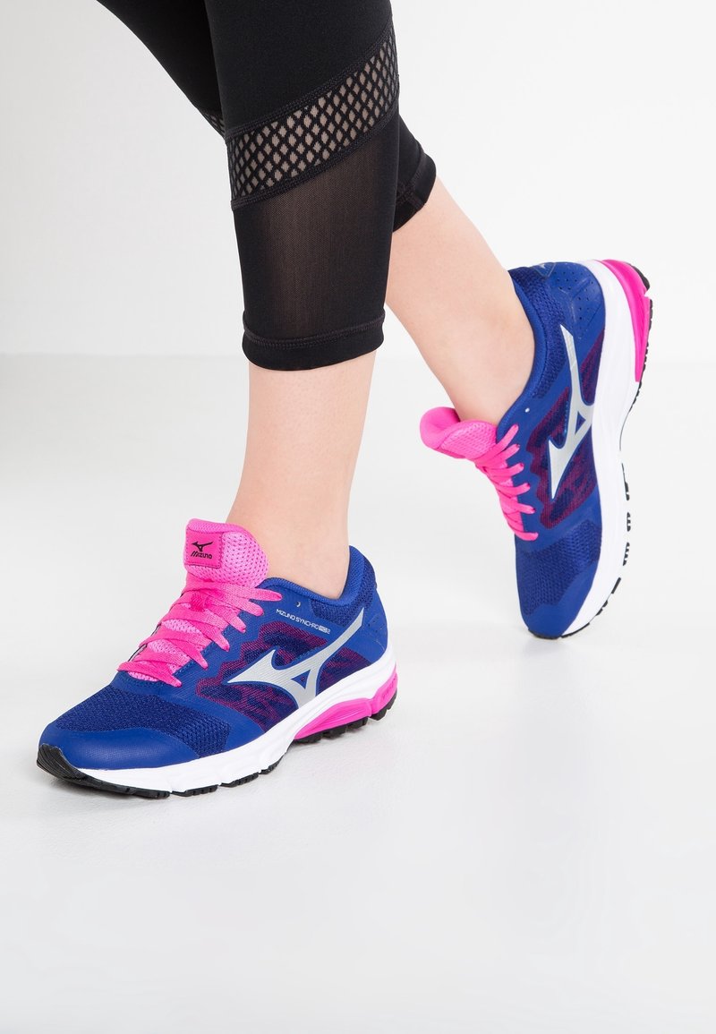 Des chaussures de sport bleues avec des accents roses et un logo argenté, avec une tige en mesh et une semelle blanche rembourrée, présentées sur un fond clair.