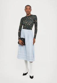 Top lung cu mâneci lungi, cu flori negre, fustă plisată de culoare albastru deschis, plic negru, șosete albe până la genunchi, și pantofi cu vârful ascuțit negri.