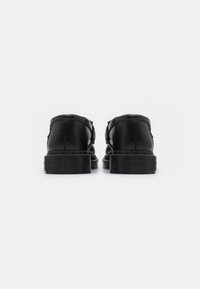 Zapatos de cuero negro con un acabado suave, forma estructurada y suela de goma texturizada. Presentan costuras mínimas y sin hardware visible.