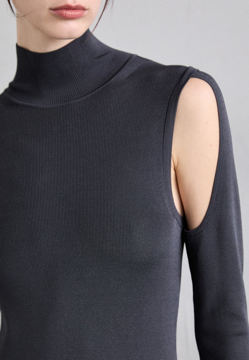 Zwarte geribbelde coltrui met een hoge halslijn, aansluitend ontwerp en uitsparing op de schouder. Zachte textuur met een verlengd linker mouw.