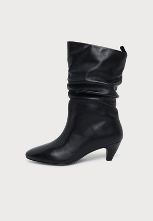 Botte en cuir noir mi-mollet avec un petit talon bas et un dessus souple, vue de côté sur un fond clair uni.