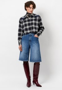 Geruite shirt in zwart en grijs met bloem borduurwerk, gecombineerd met blauwe denim culottes en bordeauxkleurige nep-krokodillen kniehoge laarzen.