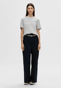 Graues Kurzarm-T-Shirt kombiniert mit lockeren marineblauen Hosen, akzentuiert durch einen hellen Gürtel und beigefarbene Schuhe. Glatte Baumwolltextur.
