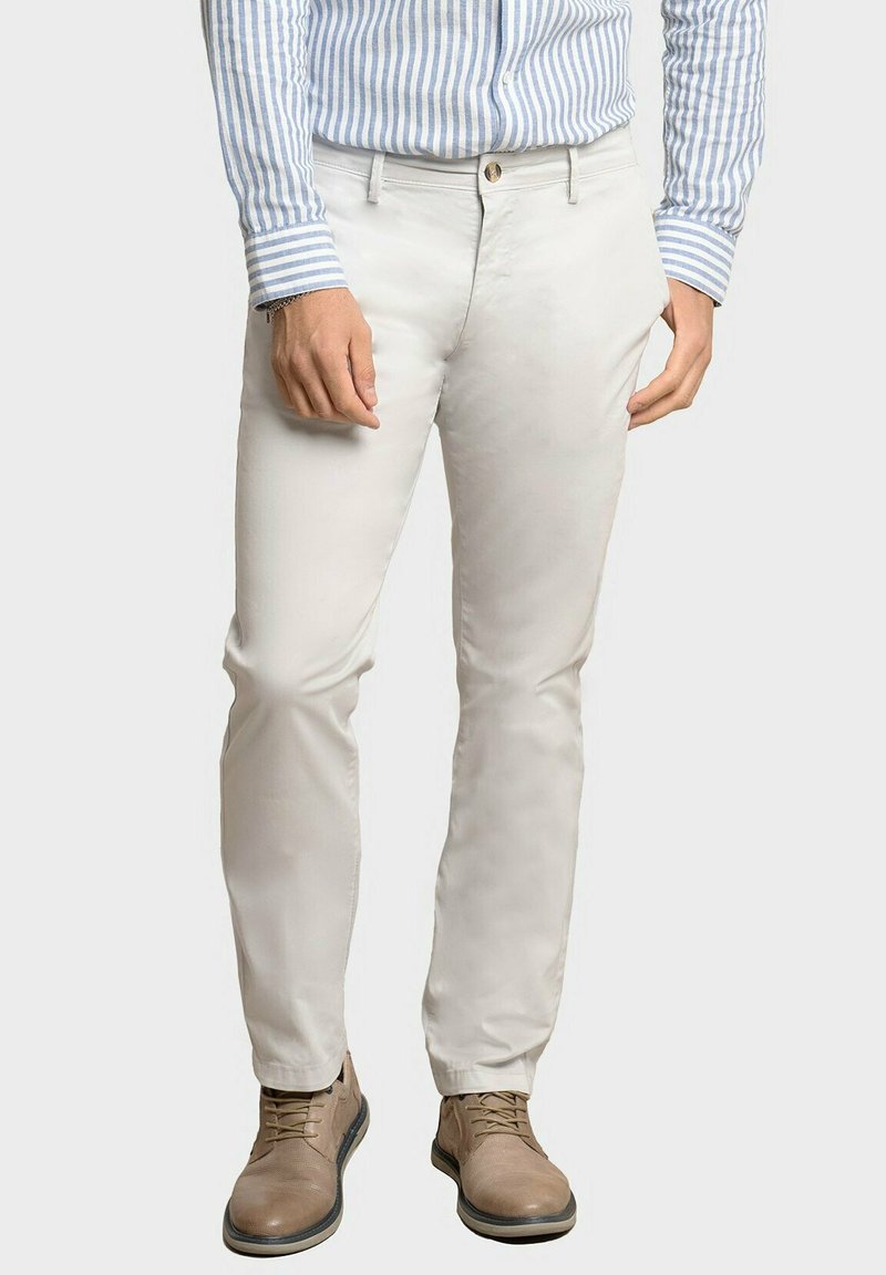 Pantalones beige hechos de una tela ligera, con un corte ajustado, bolsillos frontales y un cierre de un solo botón. Combinados con una camisa de rayas azules y zapatos marrones.