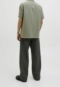Light green textured short-sleeve shirt with a button collar, paired with dark gray wide-leg trousers and black shoes.