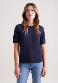 Granatowa, krótkirękawowa bluzka dzianinowa z okrągłym dekoltem, charakteryzująca się gładką fakturą i swobodnym krojem, zestawiona z jasnoniebieskimi dżinsami.