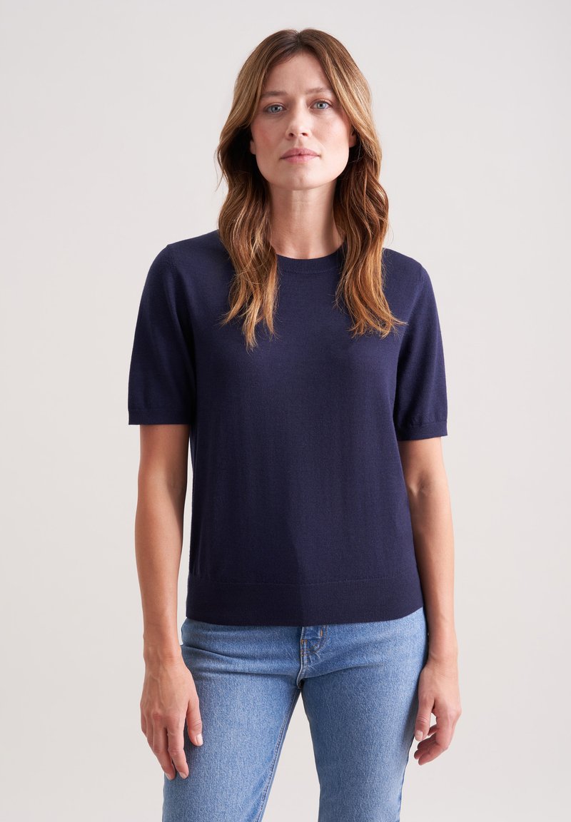 Granatowa, krótkirękawowa bluzka dzianinowa z okrągłym dekoltem, charakteryzująca się gładką fakturą i swobodnym krojem, zestawiona z jasnoniebieskimi dżinsami.