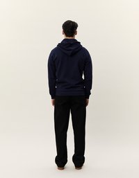 Felpa con cappuccio blu navy con cordino e tasca a marsupio, abbinata a pantaloni neri. Presenta una vestibilità rilassata e una texture morbida, vista dal retro.