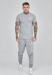 Grijze katoenen t-shirt en sweatpants set, met een ronde hals, slim fit en wit logo op de borst en dij. Witte sneakers maken de look compleet.