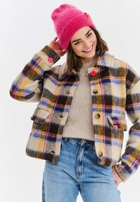 Kostkovaná vlněná bunda v béžové, žluté, modré a hnědé barvě s růžovými knoflíky a náprsní kapsou. Vytvořená v kombinaci se svetrm v světle béžové barvě a modrými džíny.