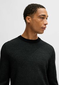 Maglione nero a maglia con un motivo testurizzato e colletto a costine. Il tessuto ha una leggera lucentezza, che mette in evidenza un design moderno.