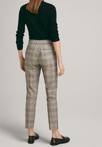 Pantalon écossais gris avec une ceinture élastique, jambe effilée, et chaussures plates noires, vu de dos avec un pull noir.
