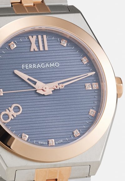Rose gold-toned watch with a blue textured dial, diamond accents, and octagonal silver case. Features slim hands and brand name "FERRAGAMO."