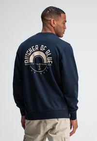 Donkerblauwe sweatshirt met ronde hals, voorzien van een groot gedrukt logo op de achterkant in lichte kleuren, en ribbelboorden aan de mouwen en onderkant.