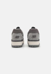 Grå suedettreningssko med en mørkegrå hælkant og svart logo bak, med en hvit mellomsåle og teksturert gummisåle.