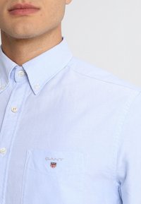 Lichtblauw overhemd van katoen met een puntig kraag, een voorklep met geborduurd "GANT" logo en witte knopen.