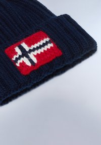 Gorro de punto azul marino con un parche de la bandera de Noruega en rojo y detalles en blanco y negro, textura acanalada y visor doblado.