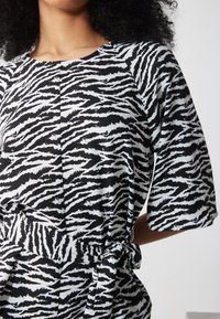 Schwarz-weißer Zebra-Print-Kleid mit kurzen Ärmeln, einem runden Ausschnitt und einer taillierten Details für eine verstellbare Passform. Glatte Stofftextur.