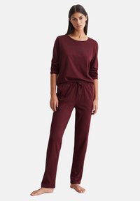 Bordeaux loungewear-sæt med lange ærmer og elastisk talje. Glat tekstur og afslappet pasform med et diskret logo på skjorten.