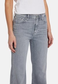 Jean en denim gris clair à coupe décontractée, taille mi-haute, cinq poches et détails de couture subtils. Texture lisse et design à jambe droite.