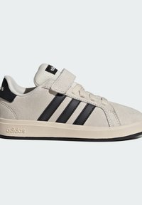 Lichtbeige suède sneaker met zwarte drie strepen, veters en klittenbandsluiting, en een gestructureerde rubberen zool. Merken op de hiel en de tong.