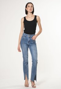 Top a righe nera senza maniche abbinata a jeans a vita alta blu chiaro con fessure frontali e dettagli di cucitura visibili.