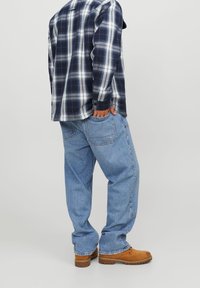 Rutig flanellskjorta i marinblått och vitt, kombinerad med löst sittande ljusblå jeans och bruna arbetsskor. Synliga sömmar och fickdetaljer.