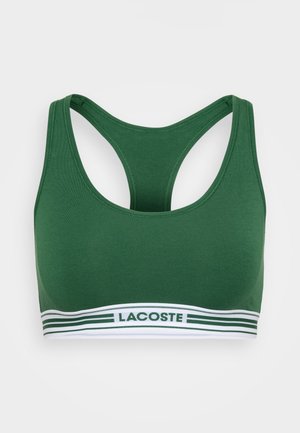 Žalias sportinis liemenėlis su lenktomis petnešomis, pagamintas iš minkštos medžiagos, su baltu dirželiu, papuoštu žaliais dryžiais ir 'LACOSTE' logotipu.