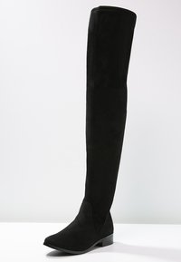 Černé kozačky nad kolena vyrobené z semiše, s užším špičatým nosem a nízkým blokovým podpatkem. Svršek je vysoký a přiléhavý, sahající nad koleno.