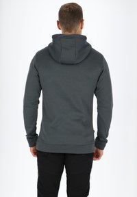 Felpa da uomo grigio scuro con finitura testurizzata, dotata di cappuccio a doppio strato e polsini a coste, abbinata a pantaloni neri.