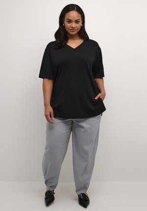 Schwarzes V-Ausschnitt-T-Shirt mit kurzen Ärmeln, kombiniert mit hellgrauen Hosen. Das Outfit zeichnet sich durch einen lässigen Schnitt und eine glatte Textur aus.