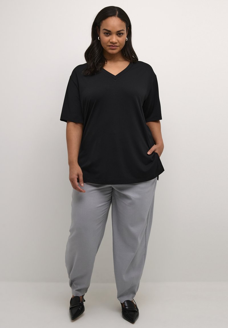 T-shirt noir à col en V avec des manches courtes, associé à un pantalon gris clair. L'ensemble présente une coupe décontractée et une texture lisse.