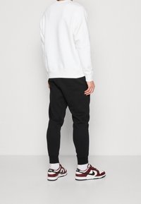 Sudadera blanca con cuello redondo, pantalones jogger negros ajustados y zapatillas deportivas en burdeos y blanco con detalles en negro.