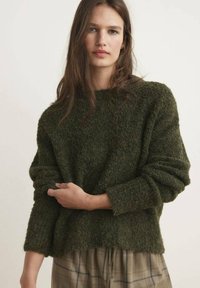 Pulover tricotat de culoare verde măslin, cu un finisaj texturat, gât larg și mâneci largi. Materialul pare moale și călduros.