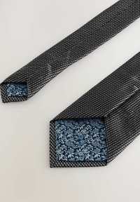 Sorte og hvide mønstrede slips med en struktureret overflade, der har en blå blomstret foring på indersiden af de spidse ender.