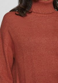 Pull à col roulé couleur rouille en tissu tricoté doux, avec un col côtelé et une coupe décontractée, offrant une texture lisse et un design épuré.