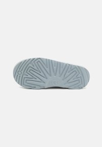 Suela de zapato de goma azul claro con patrón de tracción texturizado y logo de UGG, que presenta estrías y surcos para un mejor agarre.