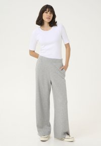 Vit figurnära t-shirt med korta ärmar i kombination med vida gråa sweatpants. Byxorna har sidofickor och en mjuk tygkänsla. Vita skor syns.